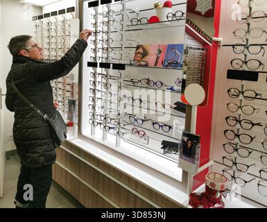 A person is looking at a display of eyeglasses in a shop. She is reaching out to pick up a pair. Displays show multiple style. Stock Photo