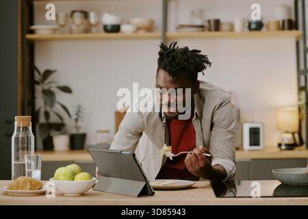 Young Black Man Eating Breakfast While Shopping Online Using Digital Tablet Stock Photo