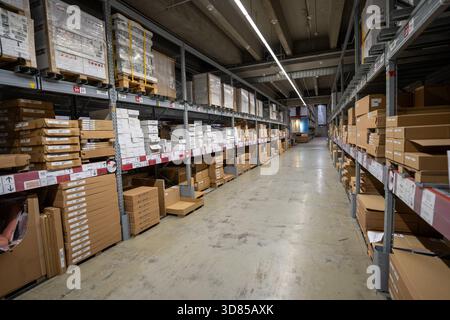 Warehouse section of an IKEA store in Germany, showing rows of tall shelves stacked with various cardboard boxes containing flat-pack furniture and ho Stock Photo