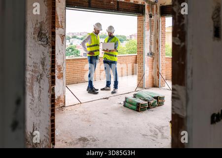 Engineers using laptop discussing project at construction site Stock Photo