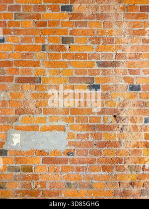 Weathered red and orange brick wall with visible mortar and patches of plaster showing signs of age and repair Stock Photo