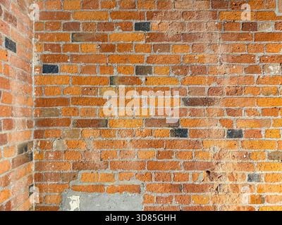 Old red brick wall with visible weathering, chipped paint and mortar variation in a corner interior or exterior surface Stock Photo