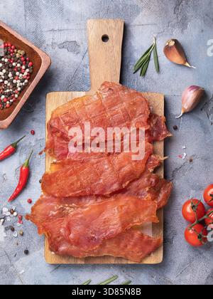 A top view of slices of dried chicken meat on a wooden tray, surrounded by various spices Stock Photo
