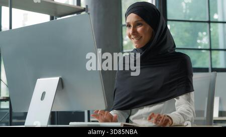 Arabian Muslim concentrated business woman in hijab working on computer in office Islamic businesswoman typing internet corporate software chatting Stock Photo