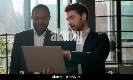 Diverse business team men colleagues cooperation with laptop online internet using web cyberspace work in office talking partners multiracial Stock Photo