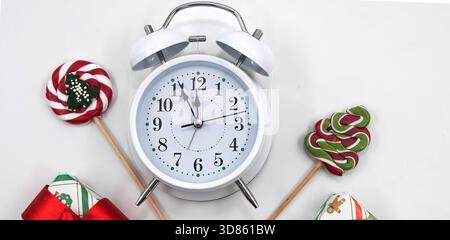 White alarm clock with festive candy and wrapped Christmas gift on white background Stock Photo