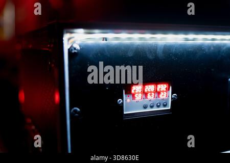 Technical equipment panel featuring a glowing red digital meter embedded in a smooth black enclosure, highlighted by overhead LED lighting and visible Stock Photo