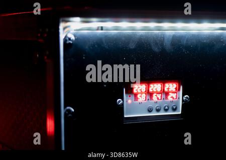 Industrial device panel displaying illuminated red numerical values on a compact digital screen, framed by metal hardware and enhanced by a bright ove Stock Photo