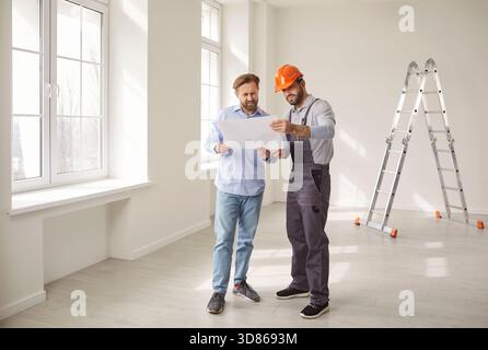 Construction team standing in empty room, reviewing blueprint and discussing renovation project. Stock Photo