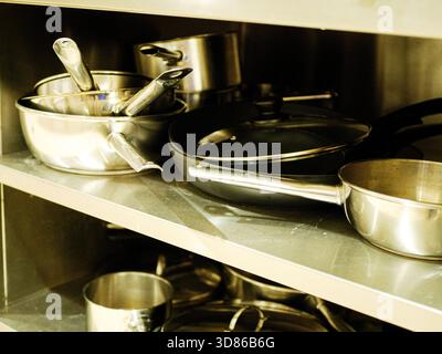 Stainless steel cookware, pans and utensils stored on metal kitchen shelf in professional restaurant environment with organised commercial cooking Stock Photo