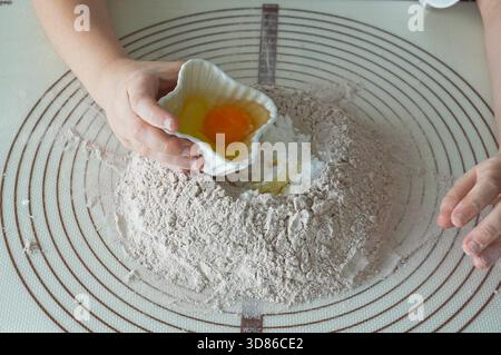 Close up of woman's hands kneading dough with egg in flour Stock Photo