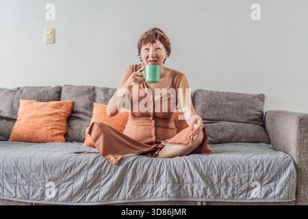 Unaltered senior woman relaxing at home and watching a comedy on TV, enjoying a cozy evening in her living room. Concept of leisure, comfort, positive Stock Photo