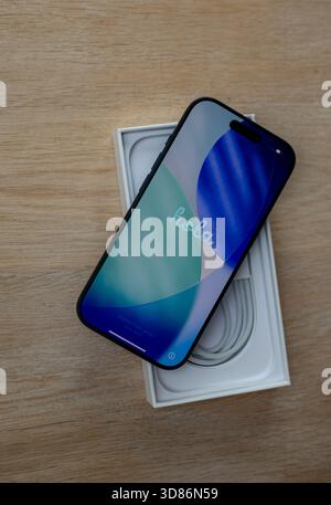 New smartphone with welcome screen resting on top of its open retail box with charging cable on wooden surface Stock Photo