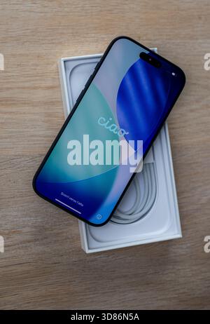 New smartphone displayed on top of its open box showing startup screen with greeting and charging cable inside the packaging Stock Photo