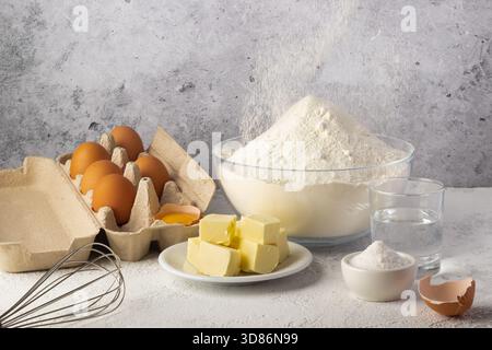 Ingredients for baking are neatly set on a kitchen counter. Eggs, flour, butter, sugar, and water are ready for mixing. A whisk hints at upcoming baki Stock Photo