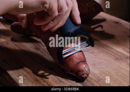 Starting to peel a sweet potato on a wood cutting board Stock Photo