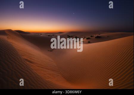 View of undulating sand dunes under a mesmerizing twilight sky, where the warm hues of sunset meet the cool blues of night, Rub' al-Khali, United Arab Stock Photo