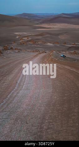 Aerial view of a winding dirt road cuts through the stark desert landscape, leading toward distant mountains under a twilight sky, Shahdad, Kerman Pro Stock Photo