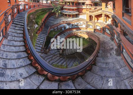 View of serpentine stairs, adorned with red railings, spiraling down into a verdant courtyard, creating a mesmerizing architectural dance, Pokhara, Ga Stock Photo