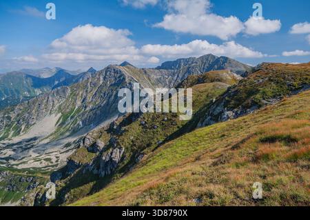View of rugged mountain peaks under a vibrant blue sky dotted with fluffy clouds, contrasting with the green and brown slopes, Bobrovec, Zilina Region Stock Photo