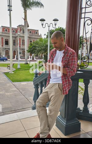 Man using smartphone in urban park, leaning, browsing social media Stock Photo