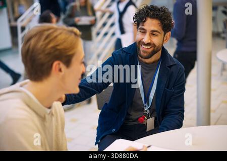 Smiling male teacher talking with student while sitting in school lobby Stock Photo
