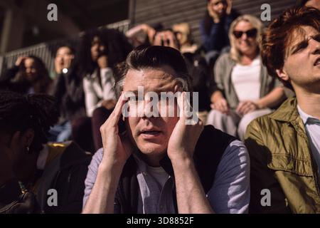 Stressed mature man touching temples while sitting in sports stadium Stock Photo