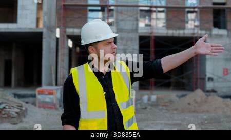 The construction worker is pointing towards an area of the site, Stock Photo