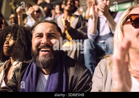 Portrait of happy man with sports scarf around neck sitting in stadium on sunny day Stock Photo