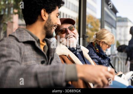 Happy senior man talking with son while waiting at bus stop Stock Photo