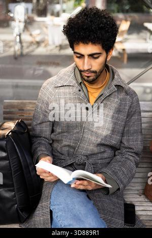 High angle view of concentrated man reading book while sitting at bus stop Stock Photo