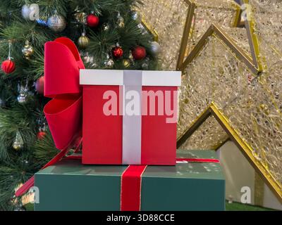 Red and green gift boxes with ribbons and a large bow are placed next to a decorated Christmas tree and golden star. Stock Photo