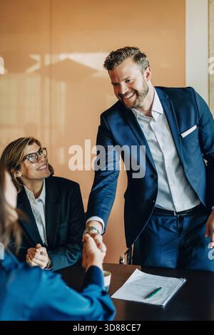 Smiling male business professional shaking hands with female colleague during deal in law firm Stock Photo