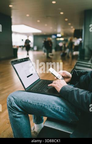 Midsection of female business freelancer using wireless technologies while sitting at airport terminal Stock Photo