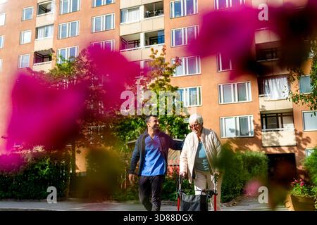 Low angle view of male healthcare worker with senior woman walking using rollator in park at sunny day Stock Photo