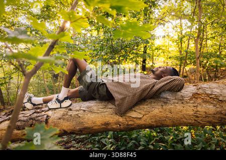 Full length of man lying on tree trunk in forest Stock Photo