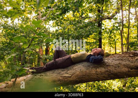 Carefree woman relaxing on tree trunk in forest Stock Photo