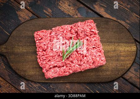 Fresh raw groundmeat with rosemary and thyme on dark wooden board over rustic table ideal for cooking, butcher and protein ingredient themes Stock Photo