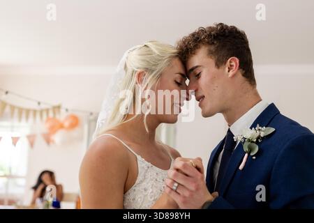 Bride and groom sharing intimate dance, smiling and holding hands at reception. Wedding, celebration, romance, couple, happiness, love || Model released Stock Photo