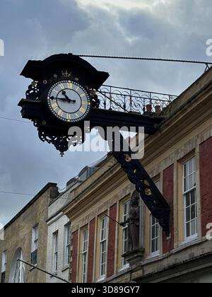 Ornate Black and Gold Public Clock on a Historic Red Brick Building in a City Street, Winchester, UK Stock Photo