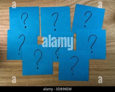 Many Blue Question Marks on Wood - Seven blue sticky notes with hand-drawn question marks lie scattered on a wooden table, symbolizing confusion, quer Stock Photo