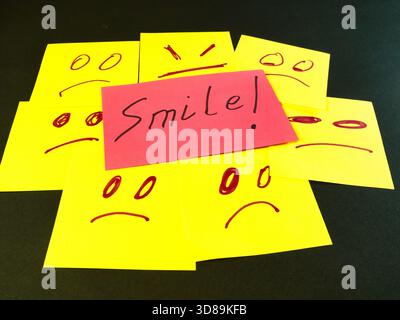 Smile! Overcoming Sadness - Red sticky note with 'Smile!' message sits atop a pile of yellow notes depicting sad and angry faces, symbolizing positivi Stock Photo