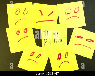 Optimism Amidst Negativity Sticky Notes - A central yellow sticky note with 'Think Positive!' message surrounded by several yellow notes displaying sa Stock Photo