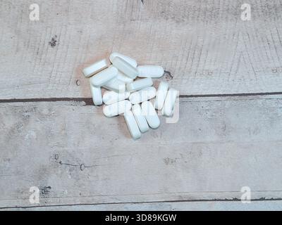 White Pills on Wooden Texture Surface - Pile of white oblong medication pills, some marked IH25, scattered on a light textured wooden surface. Health, Stock Photo