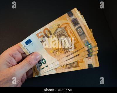 Hand Holding Fifty Euro Banknotes - Close-up of a hand holding and fanning out multiple 50 Euro banknotes against a dark background. Symbolizes financ Stock Photo