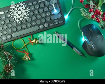 Festive Work Setup with Keyboard - Flat lay of a computer keyboard adorned with Christmas decorations and fairy lights on a vibrant green background, Stock Photo
