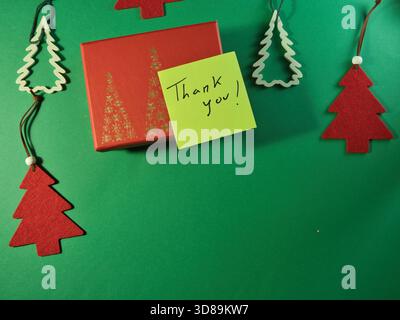 Festive Thank You on Green Background - Flat lay of a red holiday gift box featuring gold Christmas tree designs, a "Thank you!" note, and decorative Stock Photo