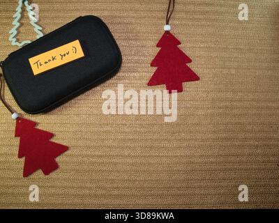 Festive Thank You with Christmas Decor - A thoughtful 'Thank You' note on a black protective case, adorned with festive red felt Christmas tree orname Stock Photo
