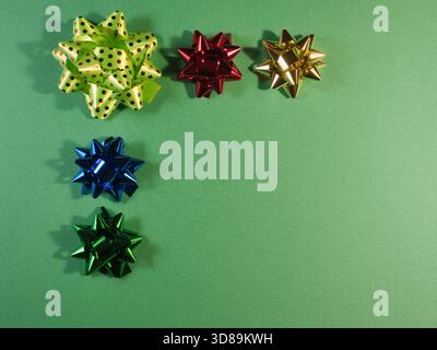 Colorful Gift Bows on Green Background - Five vibrant, metallic gift bows in various colors and designs, including polka dots, on a textured green pap Stock Photo