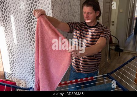 Male individual is folding a pink towel in a contemporary home setting, highlighting the significance of household chores and organized Stock Photo